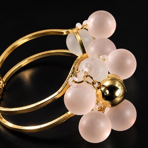 May include: A gold-toned bracelet with a cluster of pink and clear beads. The bracelet has a hinged design with three parallel bands. A large gold bead is centered in the cluster.