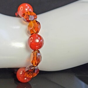 May include: A beaded bracelet featuring a mix of red and amber-colored beads. The bracelet is composed of round and faceted beads, strung together to create a vibrant accessory. The bracelet is displayed on a white surface.