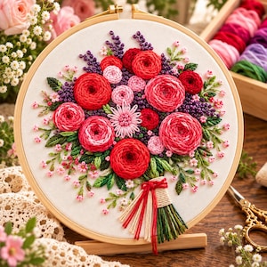 May include: A circular wooden embroidery hoop containing a fabric panel with a hand-stitched floral bouquet. The design features red and pink roses, small purple sprigs, and green leaves, with a tied stem base made of red and cream yarn threads.