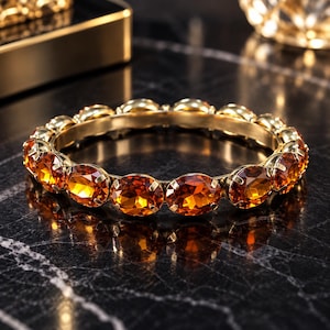 Könnte beinhalten: Ein kreisförmiges, goldfarbenes Armband mit einer durchgehenden Reihe facettierter, ovaler bernsteinfarbener Edelsteine. Jeder Stein ist in einer Krappenfassung sicher gehalten, was ein einheitliches, verlinktes Design ergibt.