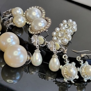 Pode incluir: Uma variedade de brincos de pérolas em vários estilos. Inclui brincos de pérola grandes, pingentes em forma de gota e brincos com detalhes de strass. Alguns brincos têm armações de metal prateado, e outros apresentam um design de tartaruga.
