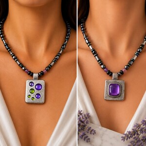 May include: Two necklaces featuring dark metallic beads and small purple accents. The left necklace has a rectangular pendant with embedded purple and green circular stones. The right necklace has a square pendant with a single large purple stone.