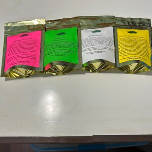 May include: Four gold foil pouches with colorful labels. The labels are pink, green, white, and yellow, each with text and a small illustration. The pouches are for different types of cleansers, including blood, intracellular, lymphatic, and gut/cell.