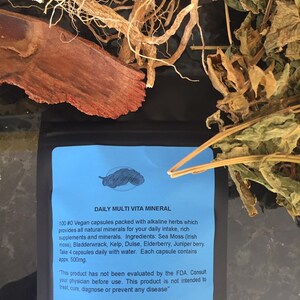 May include: A blue and white label with the text "DAILY MULTI VITA MINERAL" and information about a vegan supplement containing alkaline herbs and minerals. The label is on a black background with dried herbs and roots.