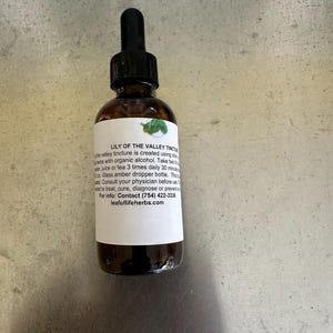 Pode incluir: Uma garrafa de vidro castanho com um conta-gotas preto. O rótulo diz "LILY OF THE VALLEY TINCTURE" e fornece instruções de uso. A garrafa contém um líquido, provavelmente um remédio herbal.