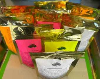 Puede incluir: Una colección de bolsas selladas de color dorado llenas de un suplemento nutricional. Las bolsas son de varios colores brillantes, incluyendo rosa, amarillo y naranja. Una bolsa tiene el texto "PARASITE CLEANSER" impreso.