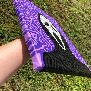May include: A purple and black canvas painting with a white ghost face in the center. The background is a swirling pattern of purple and black.