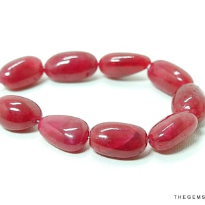 May include: A strand of ten oval-shaped, red gemstone beads. The beads are strung on a silver wire.