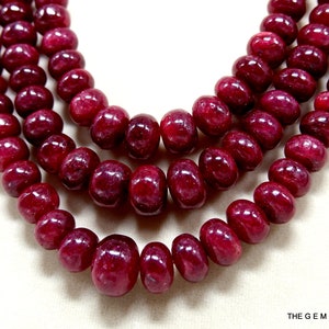 Puede incluir: Una hebra de cuentas de rubí rojo intenso, con un acabado liso y pulido. Las cuentas son redondas y ligeramente alargadas, creando un aspecto único y elegante.