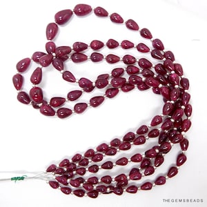 Puede incluir: Una hebra de cuentas de piedras preciosas de color rojo intenso en forma de lágrima. Las cuentas están enhebradas en un alambre plateado.