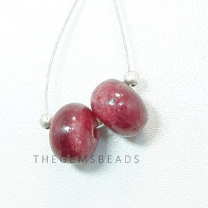 以下が含まれることがあります： 銀色の糸に通された、丸い赤い宝石のビーズが2つ。ビーズは直径約1.2cmで、滑らかで磨かれた表面をしています。