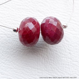 以下が含まれることがあります： 銀色のワイヤーに糸に通された、赤いルビーの宝石ビーズ2つ。ビーズはファセットカットされており、丸い形をしています。
