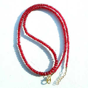 Puede incluir: Un collar de piedras preciosas rojas con un cierre de oro. El collar está hecho de pequeñas cuentas facetadas.