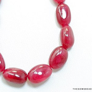 Könnte beinhalten: Eine Strähne ovaler, roter Edelsteinperlen. Die Perlen sind glatt und poliert, mit einem glänzenden Finish.