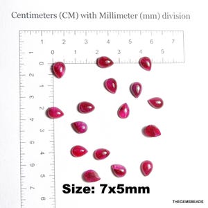May include: A collection of teardrop-shaped, polished, red gemstones. The gemstones are displayed on a white surface next to a ruler with centimeter and millimeter markings. The text "Size: 7x5mm" is visible.