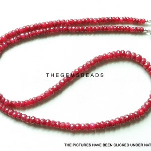 May include: A necklace of small, faceted, deep red beads. The beads are strung together, forming a double strand. A silver clasp secures the necklace. The text "THEGEMSBEADS" and "THE PICTURES HAVE BEEN CLICKED UNDER NATURAL LIGHT" are visible.