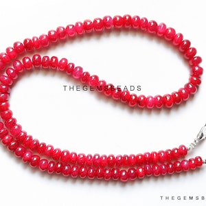 Può includere: Una collana di perle di rubino rosso vivo con chiusure argentate. Le perle sono rotonde e lisce, e la collana è lunga circa 45 cm. TheGEMSBeads è stampato su uno sfondo bianco.