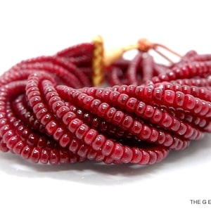 Puede incluir: Una hebra de cuentas de vidrio de color rojo intenso, cada cuenta es redonda y ligeramente alargada. Las cuentas están dispuestas en una espiral suelta, creando un diseño texturizado y visualmente atractivo.