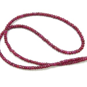 Op de afbeelding: Een streng rubijnrode edelsteen kralen. De kralen zijn gefacetteerd en hebben een licht onregelmatige vorm. De streng is ongeveer 46 cm lang.
