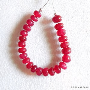 Könnte beinhalten: Eine Strähne aus 20 leuchtend roten Rubinperlen, jede Perle ist rund und leicht länglich, auf einem Silberdraht aufgefädelt.