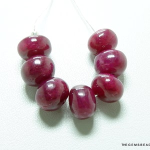 May include: A strand of seven deep red ruby beads, each bead is smooth and round, the beads are strung on a clear thread.