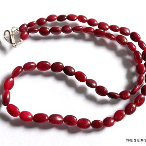 Puede incluir: Una hebra de cuentas de piedras preciosas rojas, enhebradas en una cadena de plata con un cierre. Las cuentas son de forma ovalada y tienen un acabado liso y pulido.