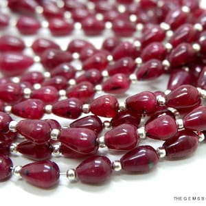 May include: A strand of deep red gemstone beads in a teardrop shape. The beads are strung on silver wire.