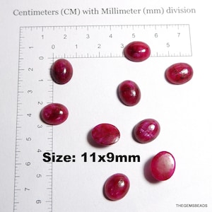 Op de afbeelding: Negen ovaalvormige, gepolijste, robijnkleurige edelstenen worden getoond op een wit oppervlak met een liniaal. De edelstenen meten 1,1 cm x 0,9 cm. De tekst "Size: 11x9mm" is zichtbaar.