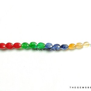 Può includere: Un filo di perle di pietre preziose ovali in rosso, verde, blu e giallo. Le perle sono infilate su un filo d'argento con una chiusura in argento. Il testo "THEGEMSBeads" è visibile nell'immagine.