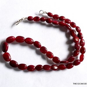 Puede incluir: Un collar hecho de cuentas de piedras preciosas ovaladas rojas con cierres plateados.