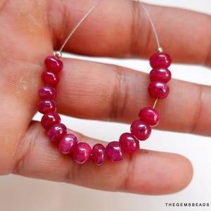 Puede incluir: Una hebra de cuentas de piedras preciosas de color rojo rubí enhebradas en un alambre de plata. Las cuentas son redondas y lisas, y todas son aproximadamente del mismo tamaño.