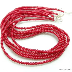 May include: A strand of red beads, made of small, round beads, strung together on a thin cord. The beads are all the same size and shape, and they are arranged in a uniform pattern. The strand is long enough to be worn as a necklace or bracelet.