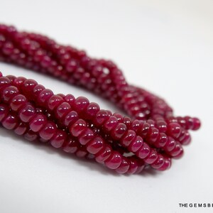 May include: A strand of deep red ruby beads. The beads are round and have a smooth, polished finish.