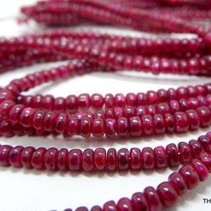 Puede incluir: Una hebra de cuentas de rubí rojo intenso, cada cuenta es redonda y ligeramente alargada, creando un aspecto texturizado. Las cuentas están enhebradas en un alambre fino, creando un collar delicado y elegante.