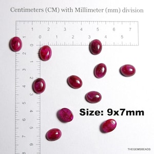 May include: A collection of oval-shaped, deep red gemstones, each approximately 9x7mm in size, are displayed against a white background. The image includes a ruler with centimeter and millimeter markings for scale. The text "Size: 9x7mm" is also visible.