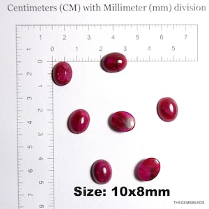 Op de afbeelding: Zes ovale, gepolijste robijn edelstenen, elk ongeveer 10 x 8 mm groot, worden getoond tegen een witte achtergrond. De edelstenen hebben een dieprode kleur met variërende interne patronen. De afbeelding bevat een liniaal voor schaal, met de tekst "Size: 10x8mm".