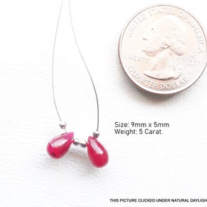 May include: A pair of earrings featuring two teardrop-shaped, deep red gemstones, each approximately 9mm x 5mm, strung on a thin silver wire. The gemstones are accented with small silver beads. A US quarter is included for size reference.