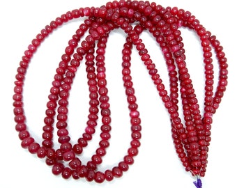 May include: A strand of deep red gemstone beads. The beads are round and have a smooth, polished finish. The strand is approximately 18 inches long.