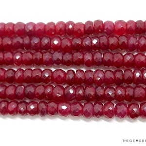 May include: A strand of red ruby beads, faceted and round, with a polished finish. The beads are strung together on a clear thread.