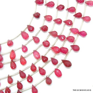 May include: A strand of red gemstone beads in a teardrop shape. The beads are strung on a silver wire and are arranged in a cascading pattern.