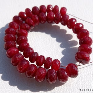 May include: A strand of deep red ruby beads, faceted and round, strung on a thin wire. The beads are arranged in a circular pattern, creating a beautiful and elegant necklace.