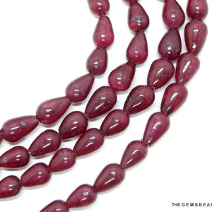Puede incluir: Una hebra de cuentas de piedras preciosas de color rojo intenso en forma de lágrima. Las cuentas son lisas y pulidas, con un acabado brillante.