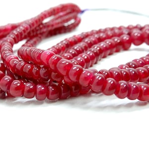 Peut inclure: Un brin de perles de pierres précieuses rouge foncé. Les perles sont rondes et lisses, avec une finition brillante. Les perles sont enfilées sur un fil fin et sont disposées en un motif lâche et fluide.