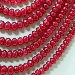May include: A close-up of a strand of bright red gemstone beads. The beads are round and smooth, and they are arranged in a symmetrical pattern. The beads are strung on a clear thread, and they are all the same size. The beads are a vibrant red colour, and they have a glossy finish.