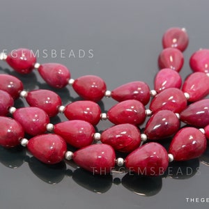 May include: A strand of deep red gemstone beads in a teardrop shape. The beads are strung on silver wire.