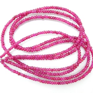 Puede incluir: Múltiples hebras de cuentas de piedras preciosas facetadas de color rosa intenso. Las pequeñas cuentas uniformes están ensartadas. Las vibrantes cuentas rosas saturadas capturan la luz, creando un efecto brillante. El fondo es blanco. Ideal para la fabricación de joyas.