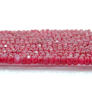 Puede incluir: Una hebra de cuentas de rubí rojo brillante, cada cuenta está facetada y tiene una forma ligeramente irregular. Las cuentas están enhebradas en un hilo fino y están listas para ser utilizadas para la elaboración de joyas.