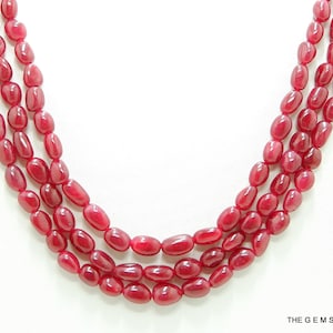 May include: Three strands of red gemstone beads, each strand is made of oval-shaped beads. The beads are strung on a clear cord.