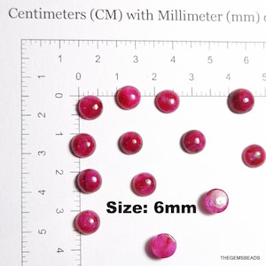 May include: A collection of round, deep pink beads, each approximately 0.24 inches in diameter, are arranged on a grid with centimeter and millimeter markings. The text "Size: 6mm" is visible. The beads are likely for jewelry making.