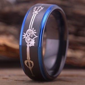 May include: A black and blue tungsten carbide ring with a silver engraved design of a heart and key.